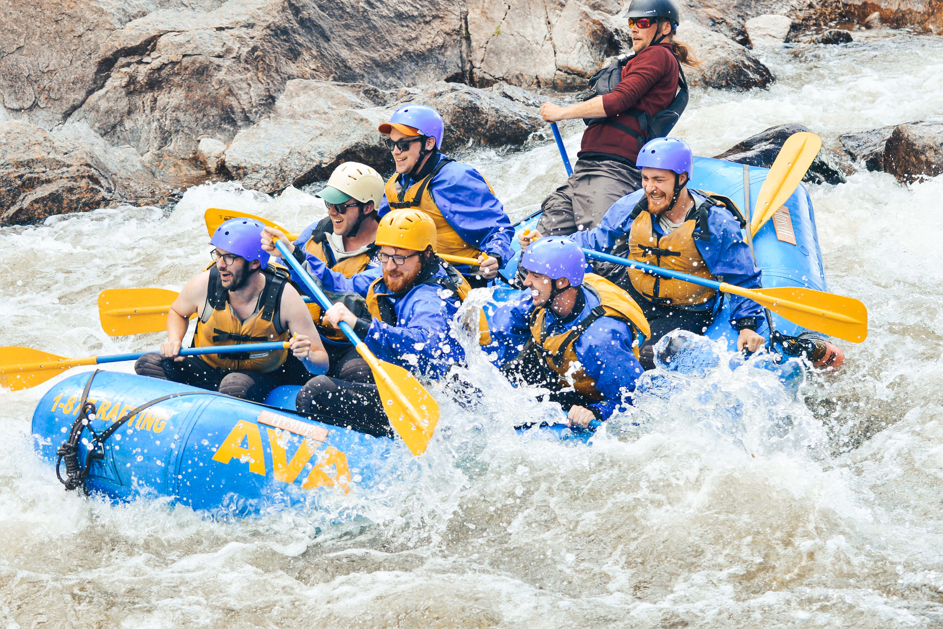 A group in a raft getting splashed while rafting through a rapid